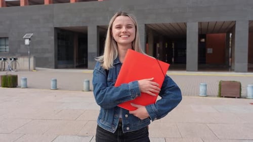 Young Female Student Smiling in a University Campus Holding a Red Folder