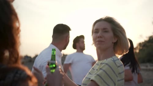 Smiling friends enjoy sunset beach party with beverages