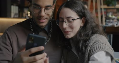 Joyful Couple African American Man and Caucasian Woman Using Smartphone Talking and Smiling in Cafe