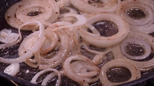 Close-up view: Rings of onion saute in hot oil in fry pan on stovetop