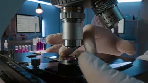 Close-up of Hands of Unknown Technologist Putting Glass Slide under Microscope