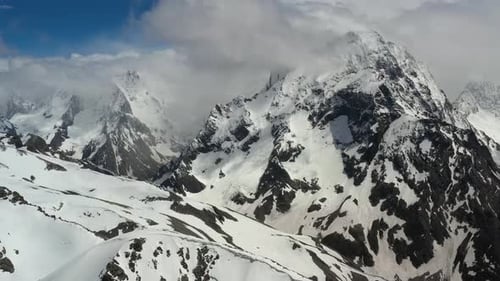 Air flight through mountain clouds over beautiful snow-capped peaks of mountains and glaciers.