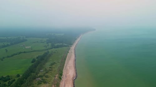 An Aerial Shot Of A Misty Green Coastal Landscape With Forests And The Waves On The Shoreline