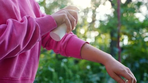 Woman Sprays Arm with Product Outside on Sunny Day