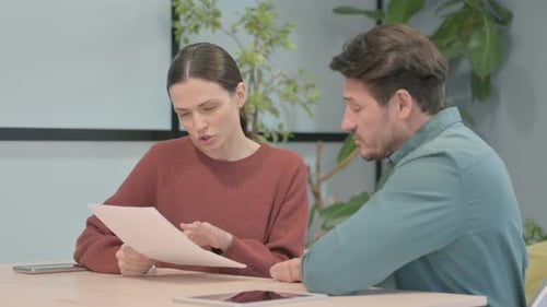 Businessman and Businesswoman Discussing Paperwork in Office