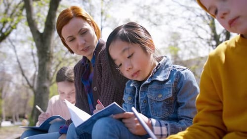 Teacher with Small Children Sitting Outdoors in City Park, Learning Group Education
