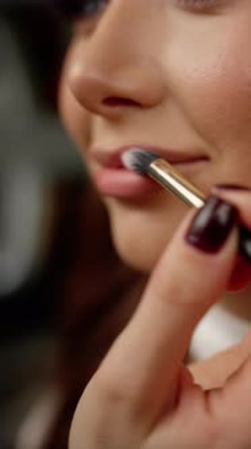 Visagist trägt mit professionellem Make-up vorsichtig tiefroten Lippenstift auf die Lippen des Models auf