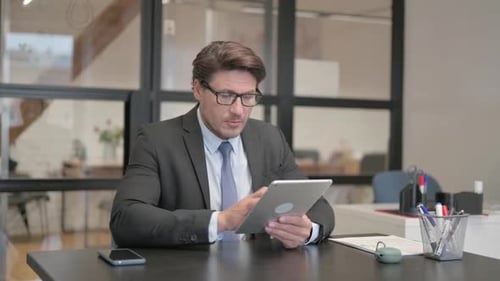 Middle Aged Businessman Using Digital Tablet in Office