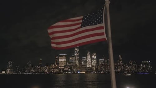 American Flag Waving Over Illuminated Urban Cityscape at Night