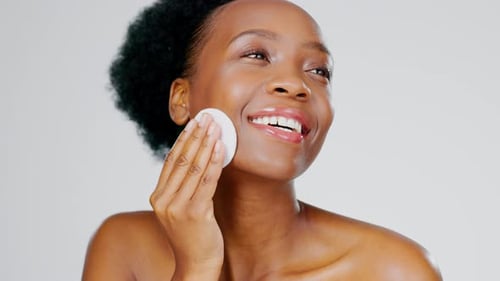 Skincare, beauty and black woman with cotton pad on face, smile and makeup