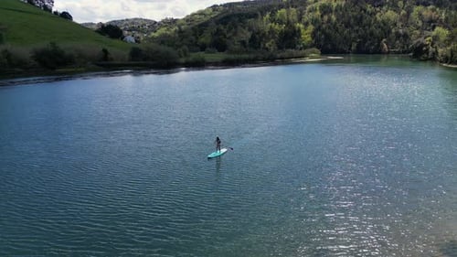 Drone aerial panning Latin woman in bikini paddle surfing towards camera on sunny summer day