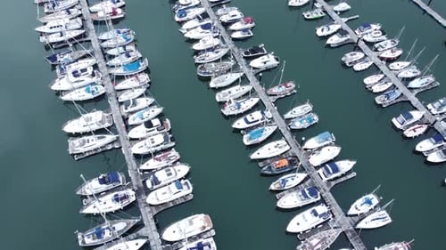 Top down aerial view above luxury yachts parked on turquoise ocean water marina rotating left