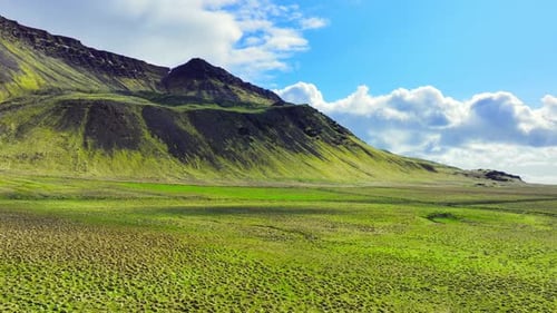 Black Volcanic Mountains with Green Grass at Spring Blue Sky with Clouds Over the Hills Magical
