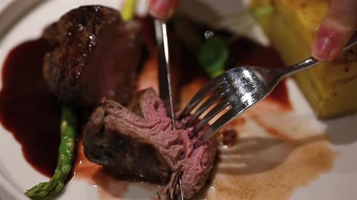 Close up of a woman cutting a juicy gourmet beef steak with knife and fork on an elegant restaurant