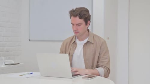 Young Man Leaving Workspace after Closing Laptop