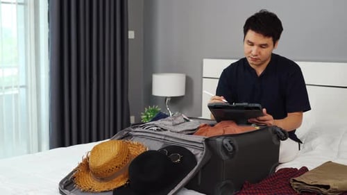 Man Packing Suitcase for Trip Using Tablet