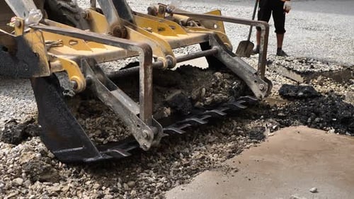 Bucket of the Excavator Breaks the Old Asphalt
