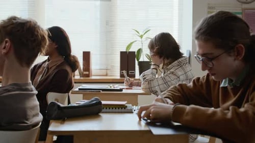 Geeky Teenage Schoolboy Writing Test with Classmates at High School Lesson