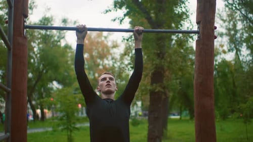 Klimmzugtraining im Freien, Sportler trainiert Klimmzüge auf einer Holzbar im Grünen, jung