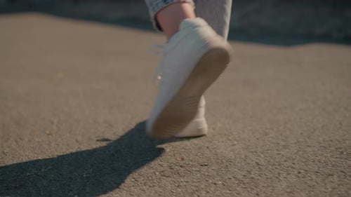 CloseUp of Legs Walking in White Sneakers on Sunlit Road with Shadows