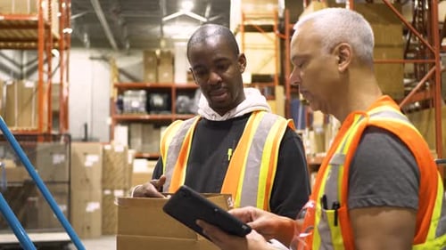 Warehouse supervisor and employee discuss inventory with digital tablet