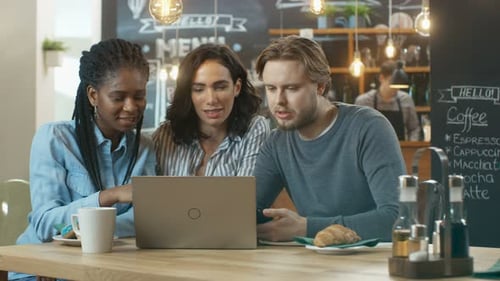 Three Young People in the Coffee Shop, They Work on a Laptop and Talk. In the Background Stylish Ca