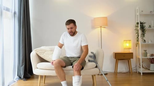 Man with Arm and Leg Casts Sits on Couch