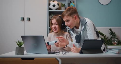 Emocionados jugadores caucásicos, niña y niño sentados junto a la mesa y jugando Vídeo en la consola