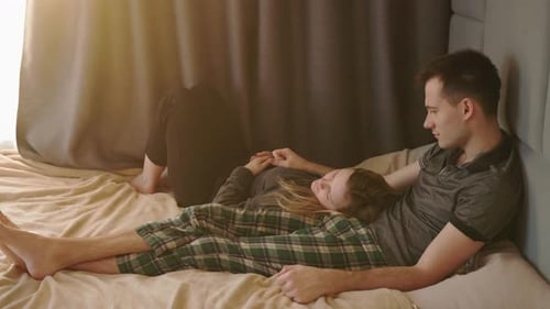 Junges Paar entspannt sich zusammen im Bett. Die Frau legt ihren Kopf auf den Schoß des Mannes, während er zuschaut
