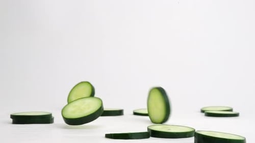 Bright green fresh cucumber slices falling, flipping and bouncing on white backdrop in slow motion