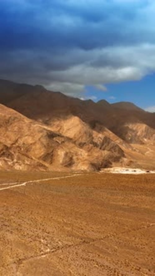 Hot plain desert limited by bare rocks. Huge cloudscape covering the mountain.