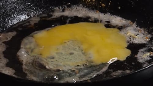 Egg broken into hot buttered cast iron pan, yellow yolk breaks, fries