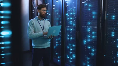 A Man Works on a Laptop in a Server Room Highlighting Tech and Data