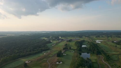 Drone over golf course fairway surrounded by trees on sunny summer day