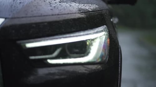 Black High End Car LED Headlight turning on in the Rain as Dew Drops form on the Hood, Extreme Close
