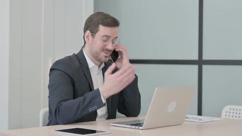 Man Working at Desk Talking on Cellphone
