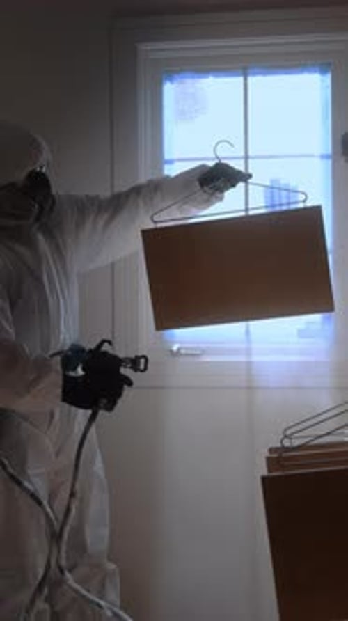 Vista vertical del trabajador que usa una pistola rociadora para aplicar pintura o revestimiento dentro del gabinete durante la renovación