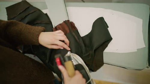 Close up of a tailor using a professional steam iron on black fabric in a fashion workshop