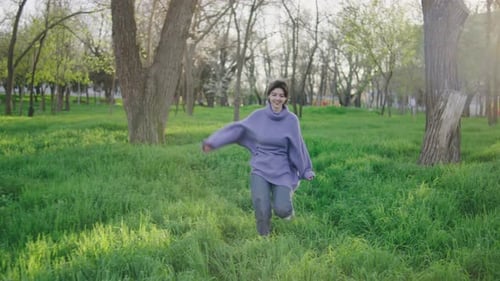 Woman Runs Joyfully in Green Park on a Sunny Day with Trees and Grass Surrounding Her in Spring