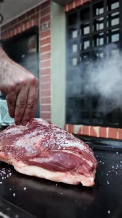 Chef salting raw meat for barbecue dinner party at home backyard. Vertical video