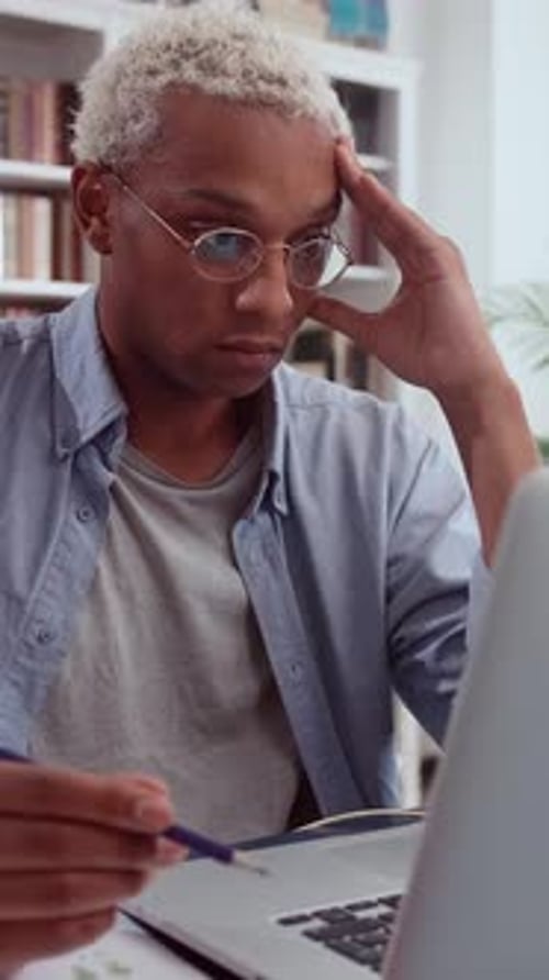 Stressed African American Student Rubs His Temple While Struggling with Difficult Task on Laptop