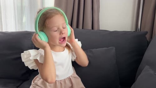 Little Girl Emotional Enjoying Music Using Green Kids Headphones in Home