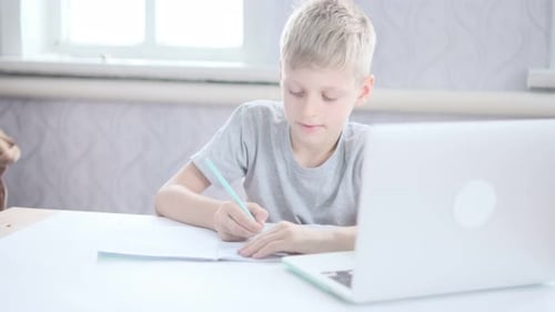 Boy Writing Homework Next To Laptop