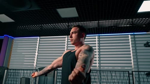 Close Up in the Gym Young Handsome Guy with Tattoos in a Black Tshirt is Doing Warmup in Front of