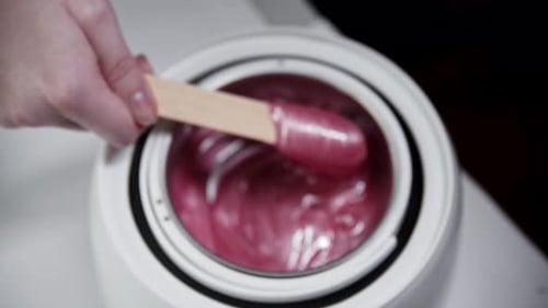 Depilation Master Melts Wax in the Heater and Mixing It Using a Spatula