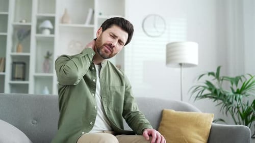 Man Sitting Massaging Neck in Pain Indoors