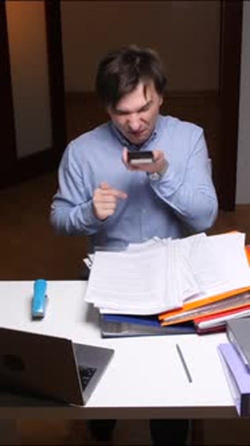 Vertical Video Stressed Office Worker Throwing Phone at Work with Folders and Laptop