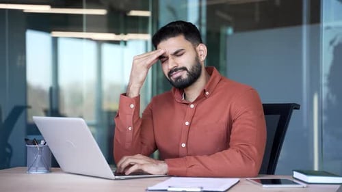 Businessman suffering from headache while working on laptop sitting at workplace in office. Upset