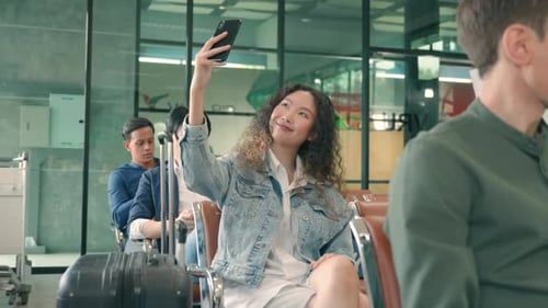 Happy Asian young beautiful woman curly hair taking selfie by smartphone at airport terminal hall