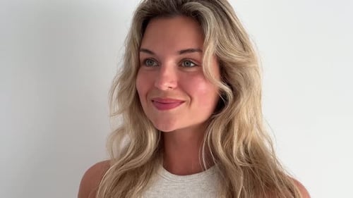 Smiling Woman Touches Hair Against White Background